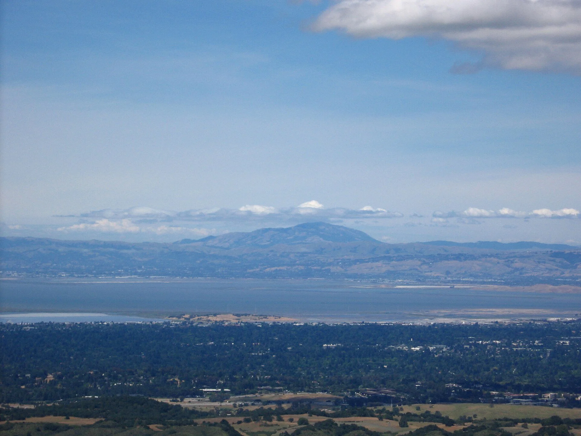Mount Diablo rising above a hazy San Francisco Bay and the cities of the Peninsula and East Bay, seen from Windy Hill under a pale blue sky.