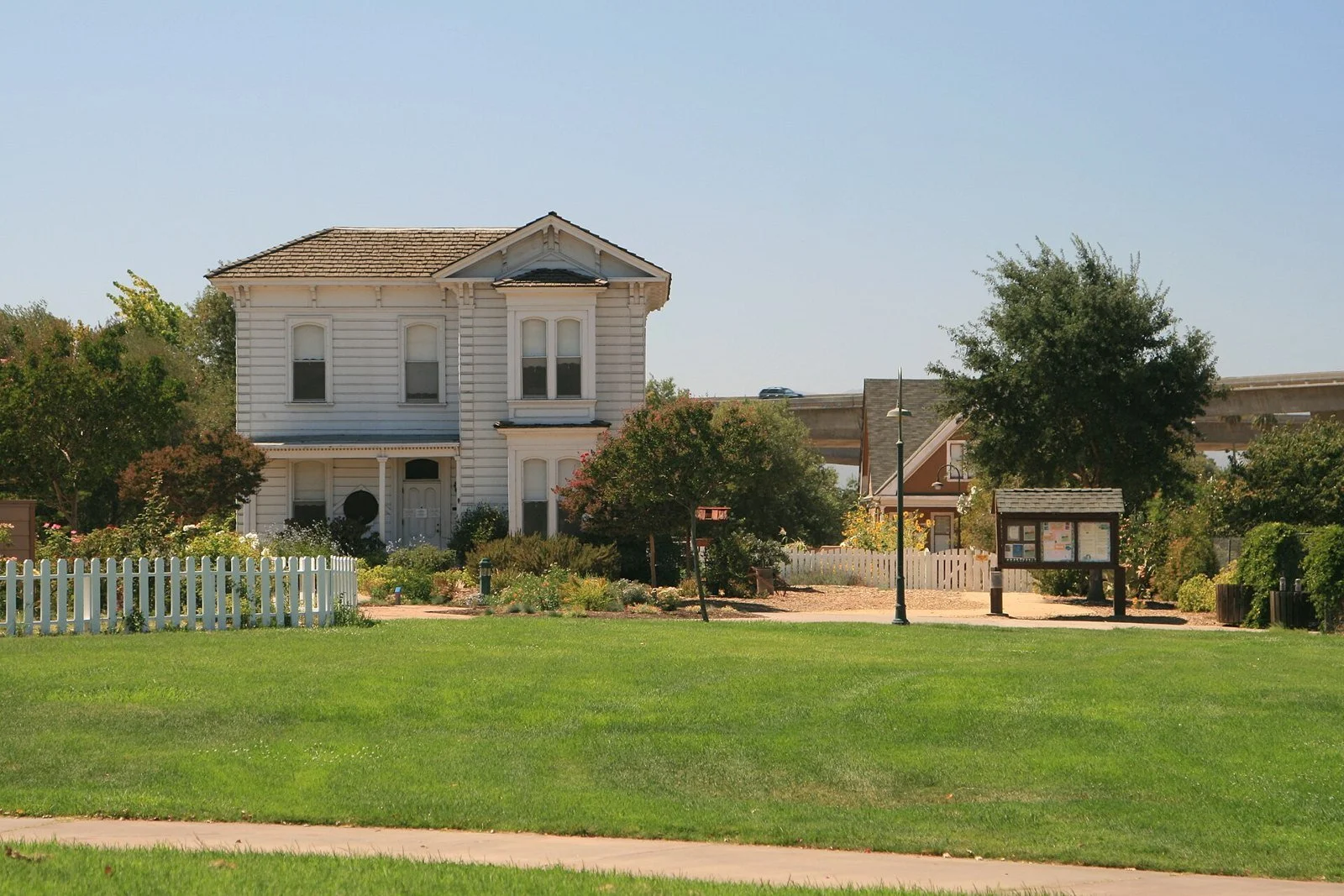 A white two-story farmhouse with a porch and picket fence behind a broad green lawn at Emma Prusch Farm Park.