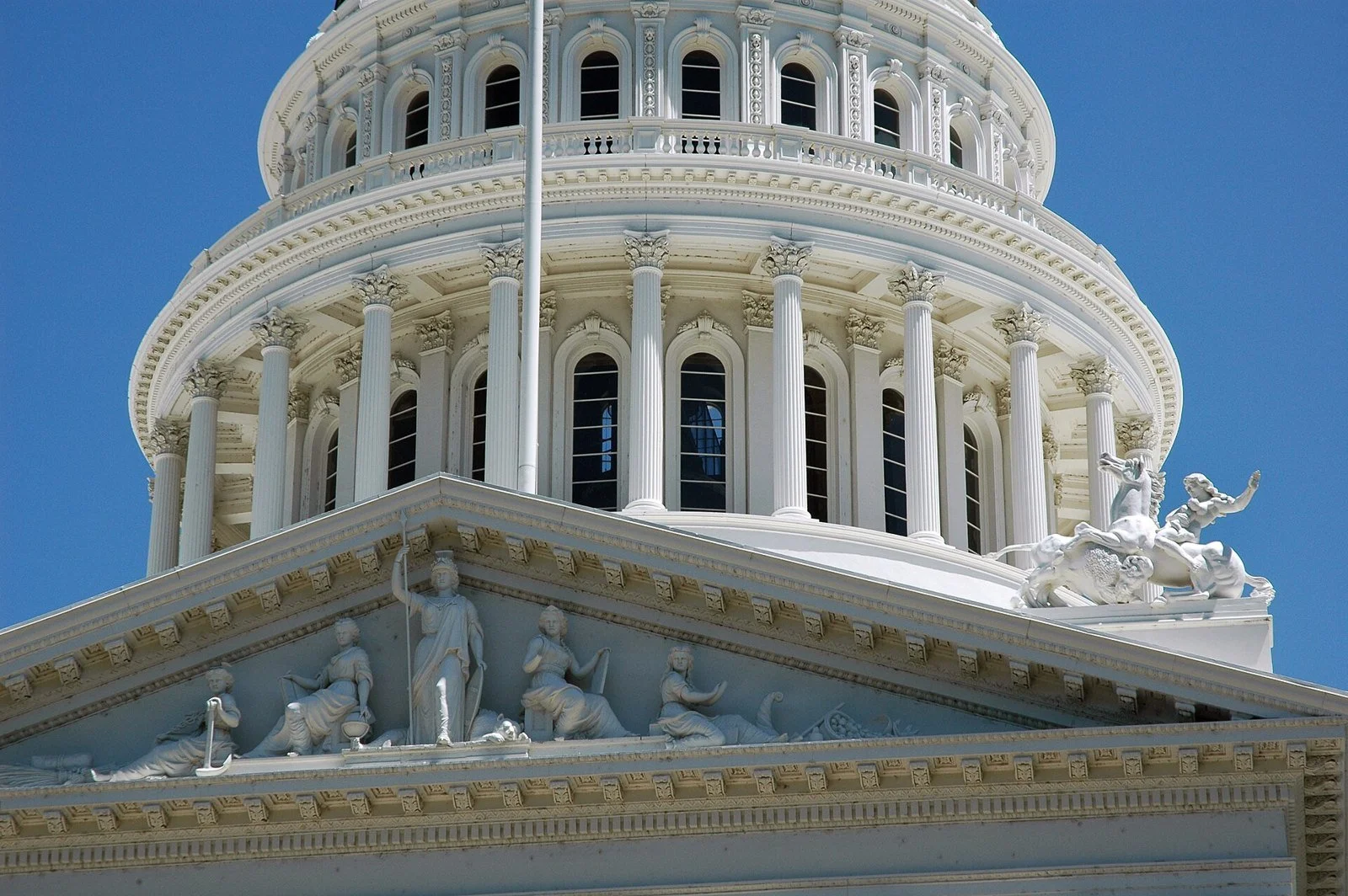 Close view of the California State Capitol's columned pediment with sculptures and its dome above.