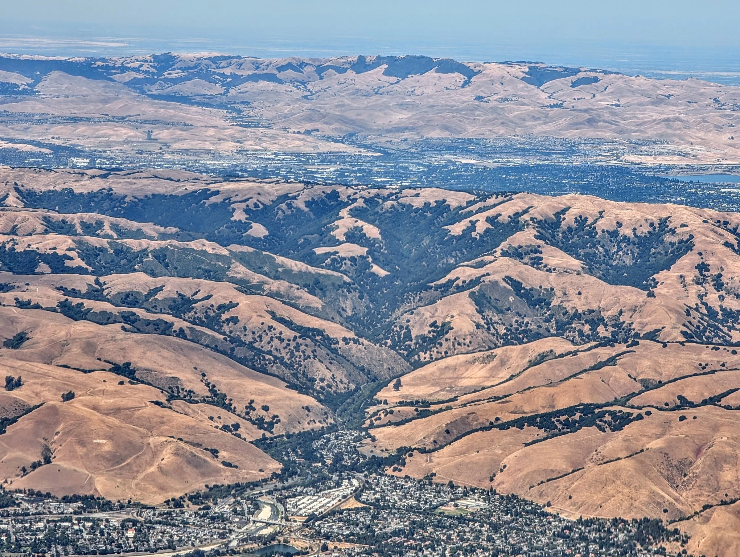 An aerial view of Niles Canyon, where Alameda Creek winds between steep, sun-browned ridges toward the Tri-Valley.