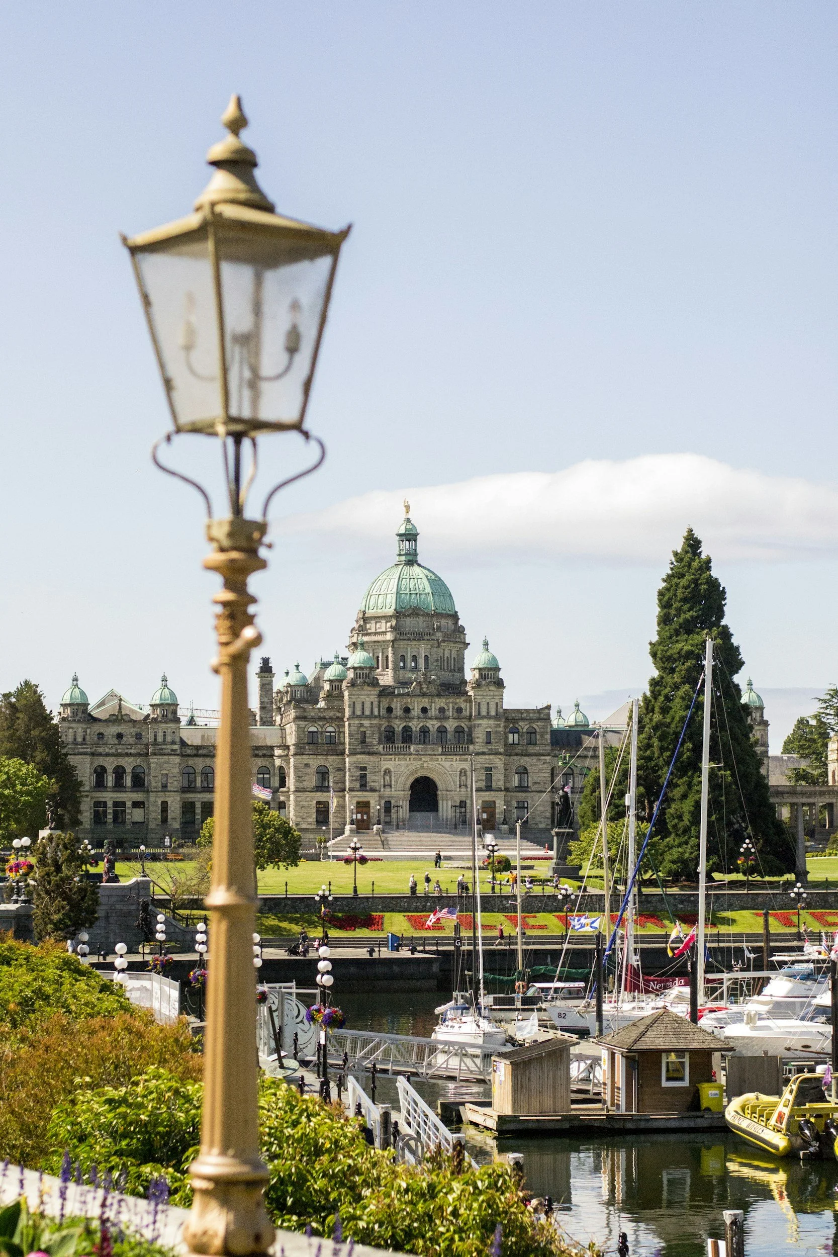 View of a historic government building with a large green dome, boats docked at a marina, and a decorative street lamp in the foreground.