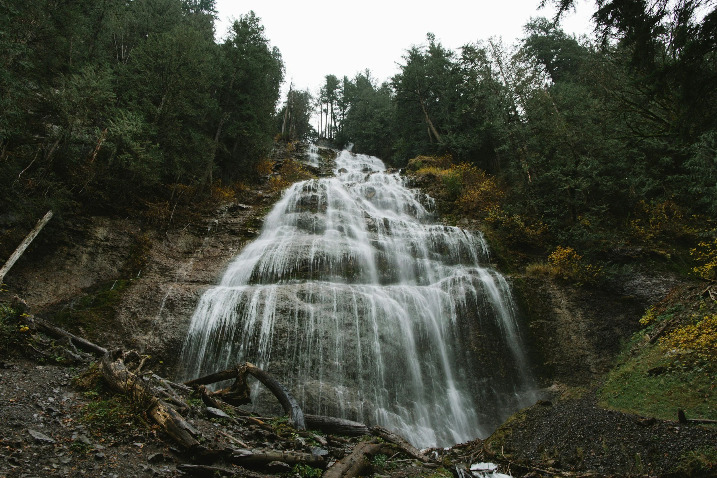 A multi-tiered waterfall flowing down a rocky cliff surrounded by green trees.