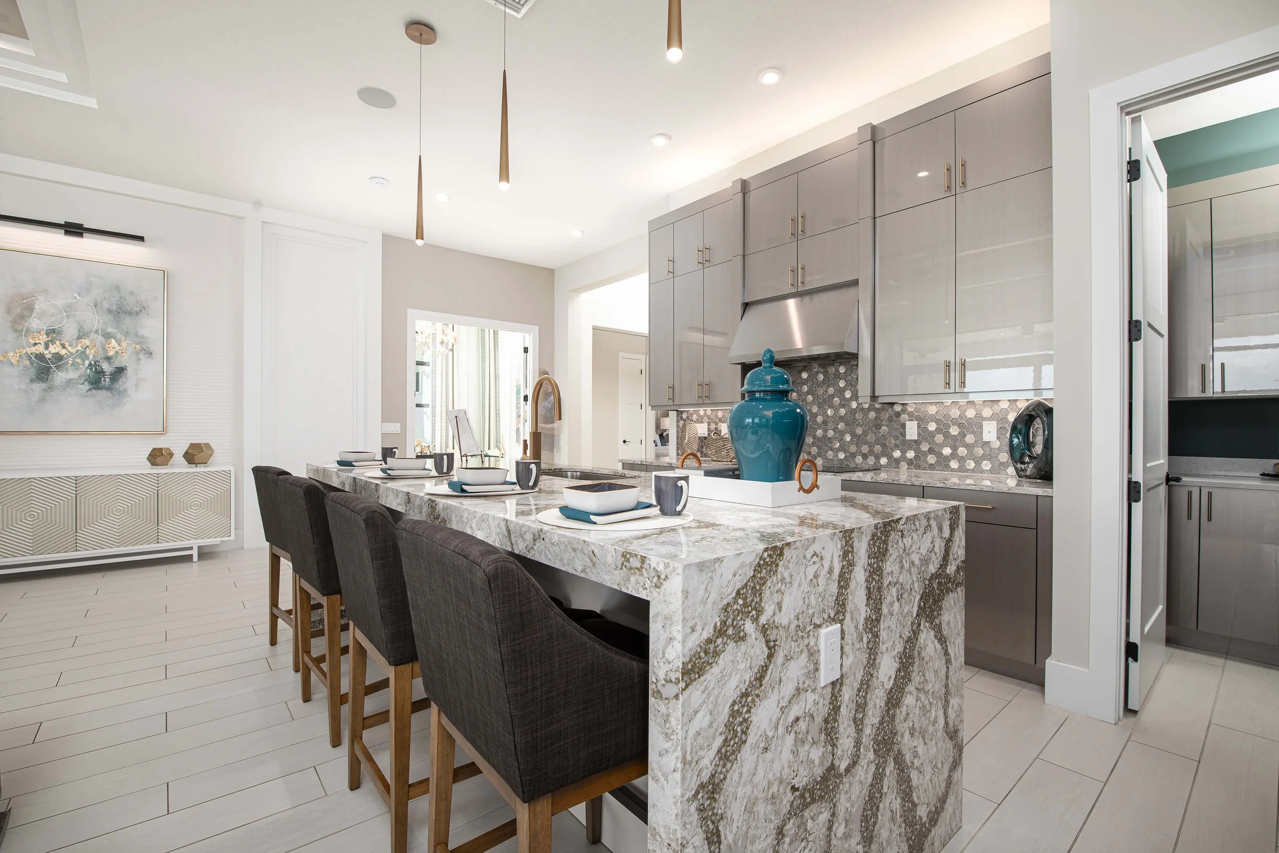 Modern kitchen with granite island, gray cabinetry, and decorative backsplash, featuring a large blue vase and table setting.