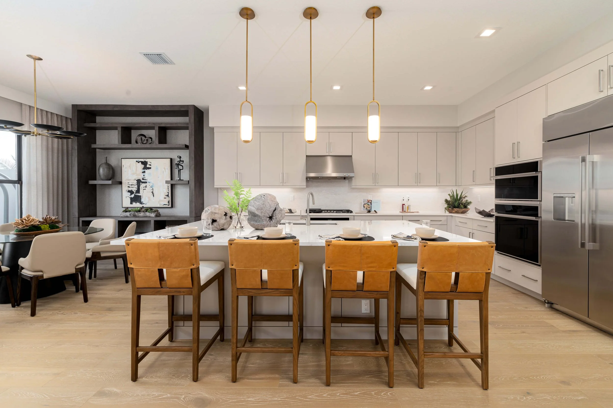 Modern kitchen with white cabinets, a large island with four yellow stools, pendant lighting, and stainless steel appliances.