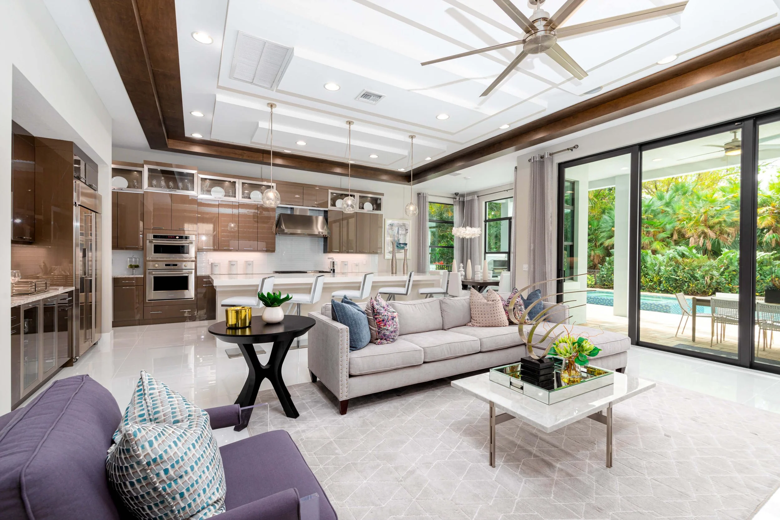 Open-concept living room and kitchen with large sliding glass doors to outdoor patio, modern furniture, and lush greenery outside.