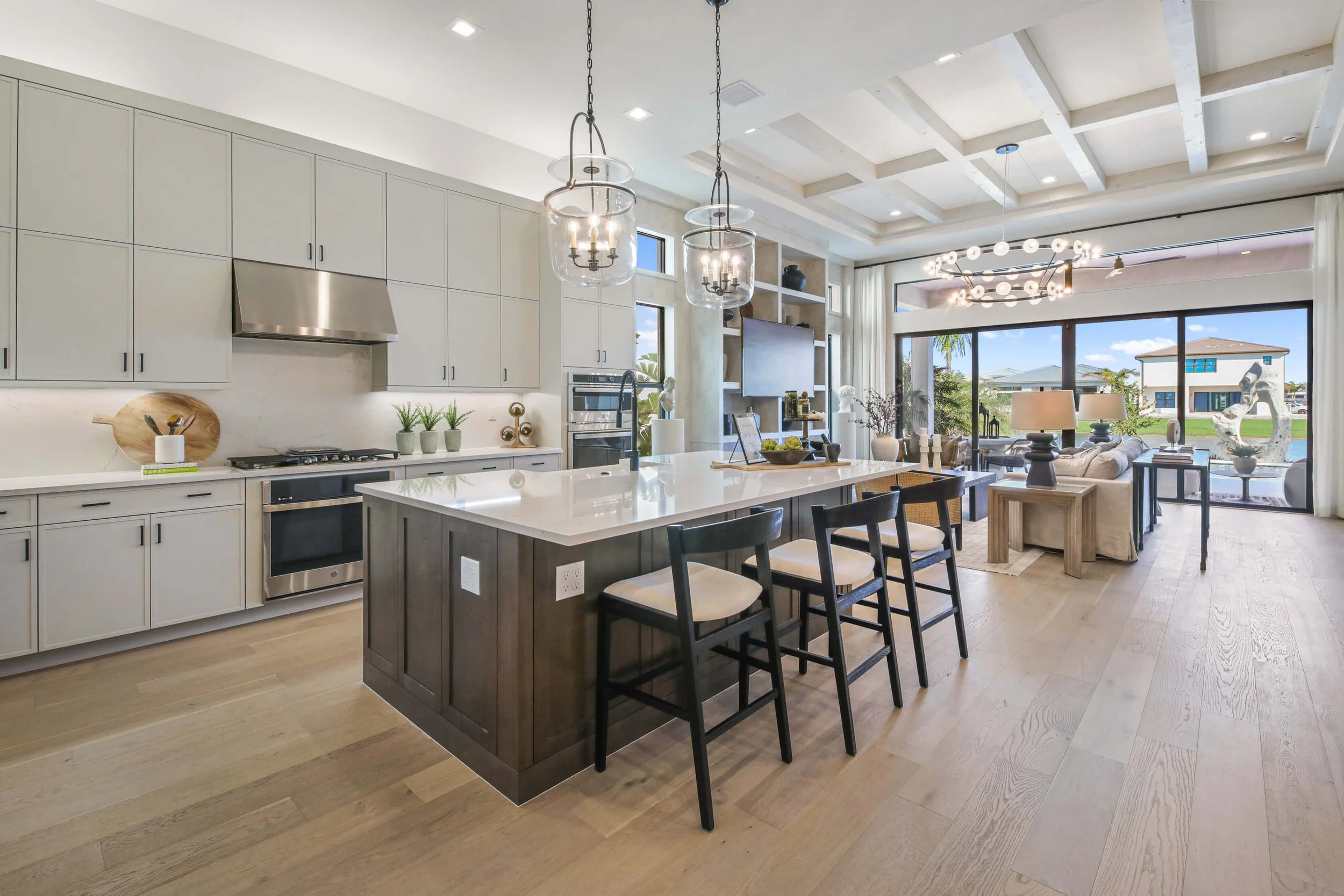 Open-concept kitchen and living room with modern decor, white cabinetry, kitchen island, pendant lights, large sliding glass doors, and views of a backyard.