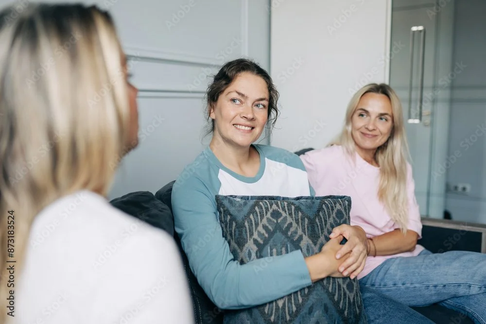 Three women sitting on a couch and engaging in conversation in a modern office or lounge setting.