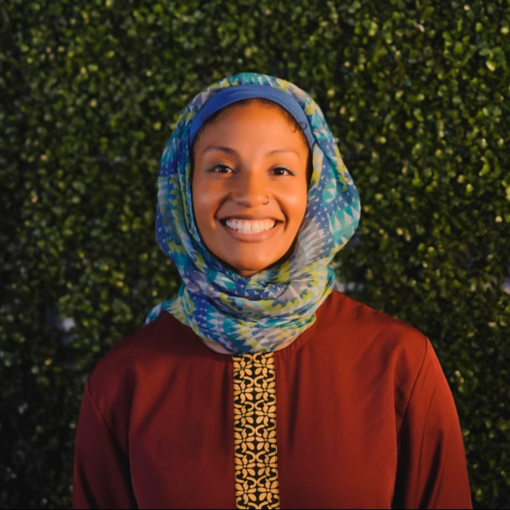 Pictute of Fatima standing in front of a green, plant wall