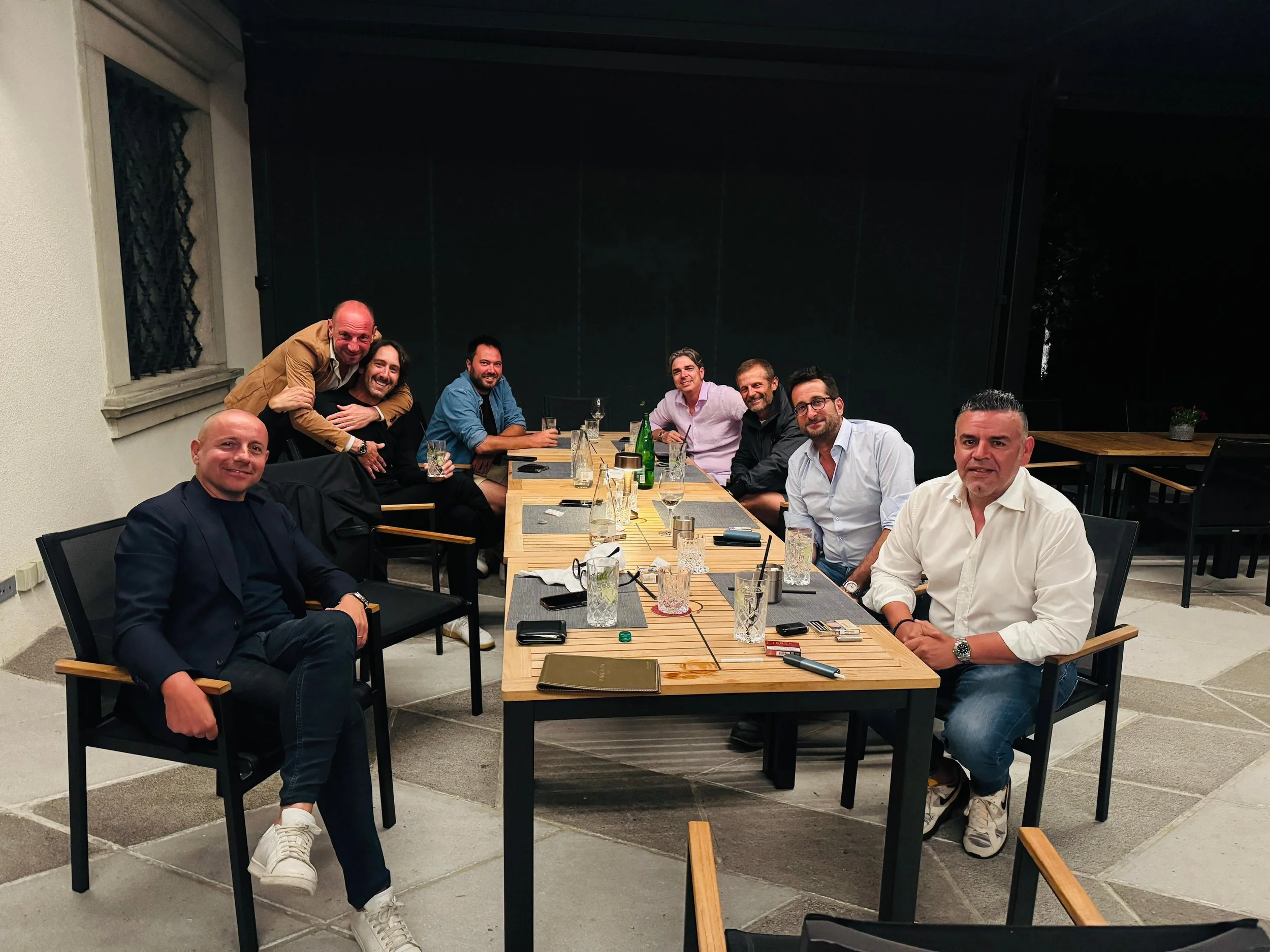 Gruppo di persone sedute intorno a un tavolo in un ristorante, sorridenti e rilassate, in un ambiente serale.