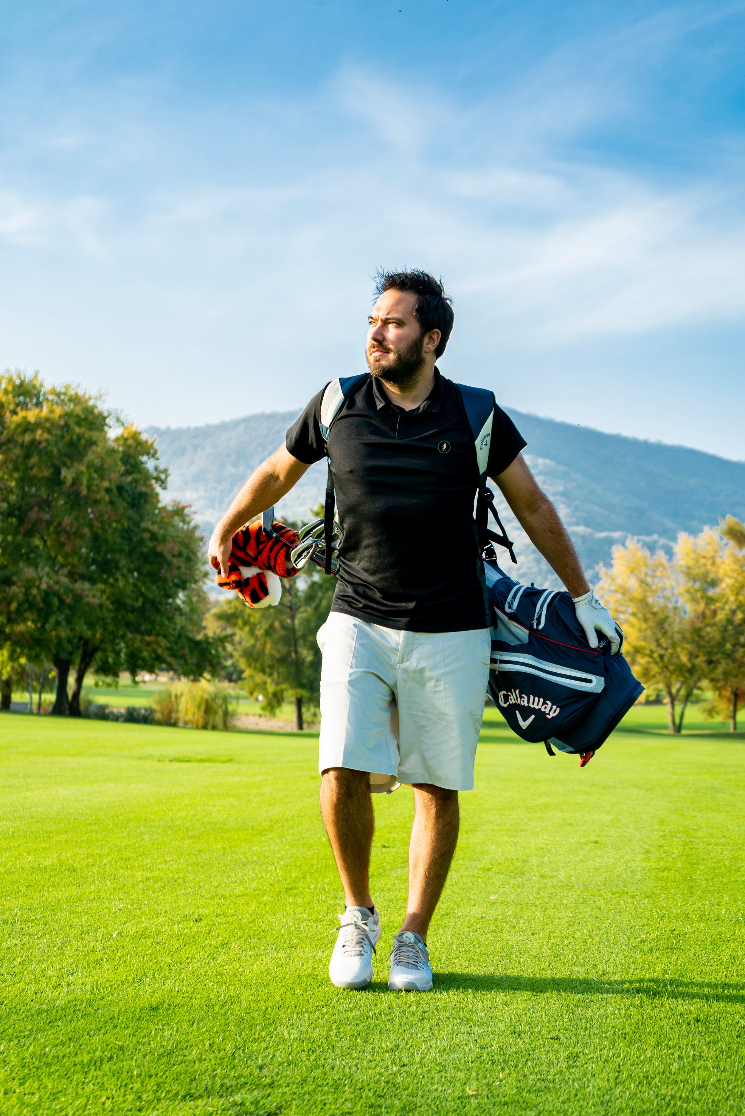 Giocatore di golf con attrezzatura, camminando sul campo da golf in una giornata soleggiata.