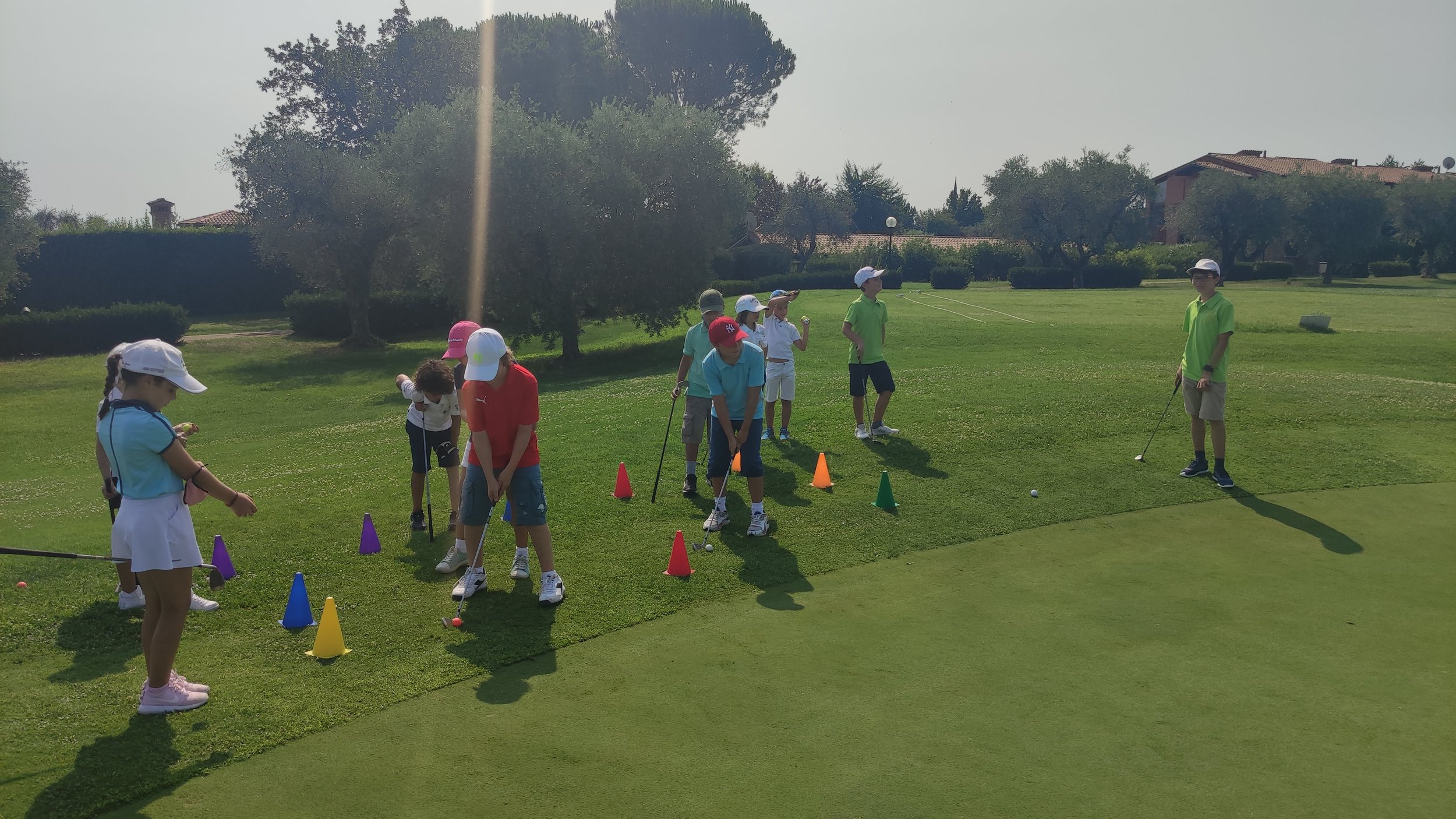 Bambini che praticano golf su un campo verde con coni colorati per esercizi.