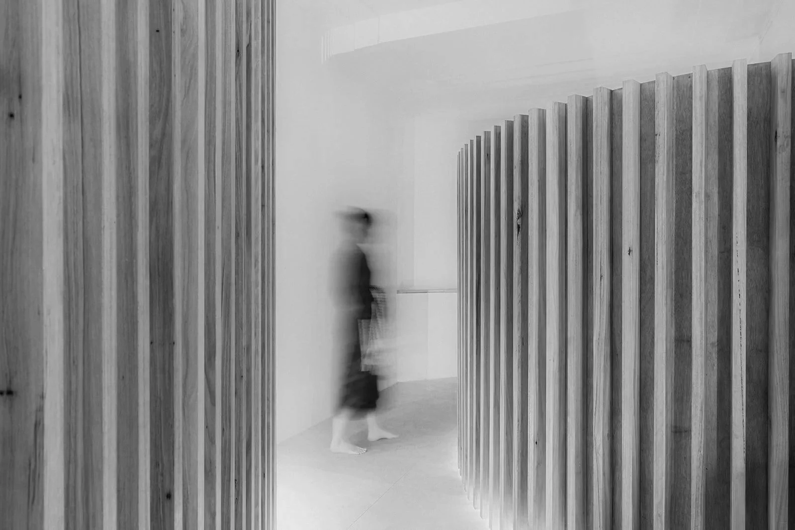 A person walking past wooden wall panels in a modern, minimalist interior with a white wall background.