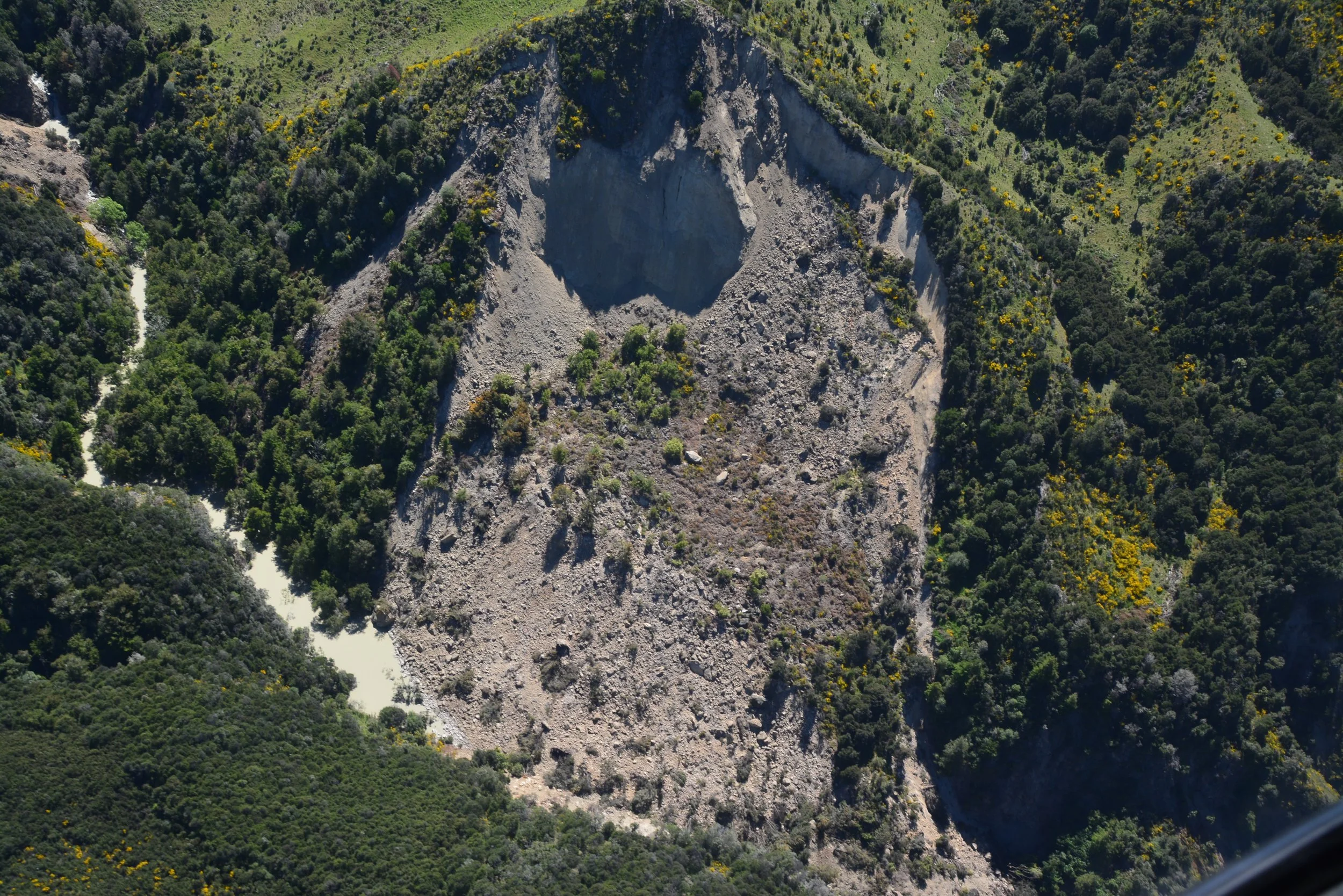 Aerial view of a large landslide covering part of a river and surrounded by bush.