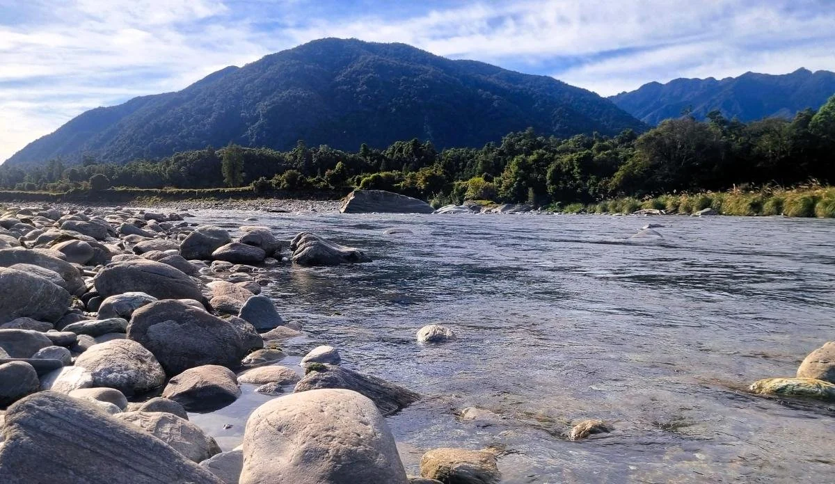 Close up photo of the Arahura river with bushy hills in the background.