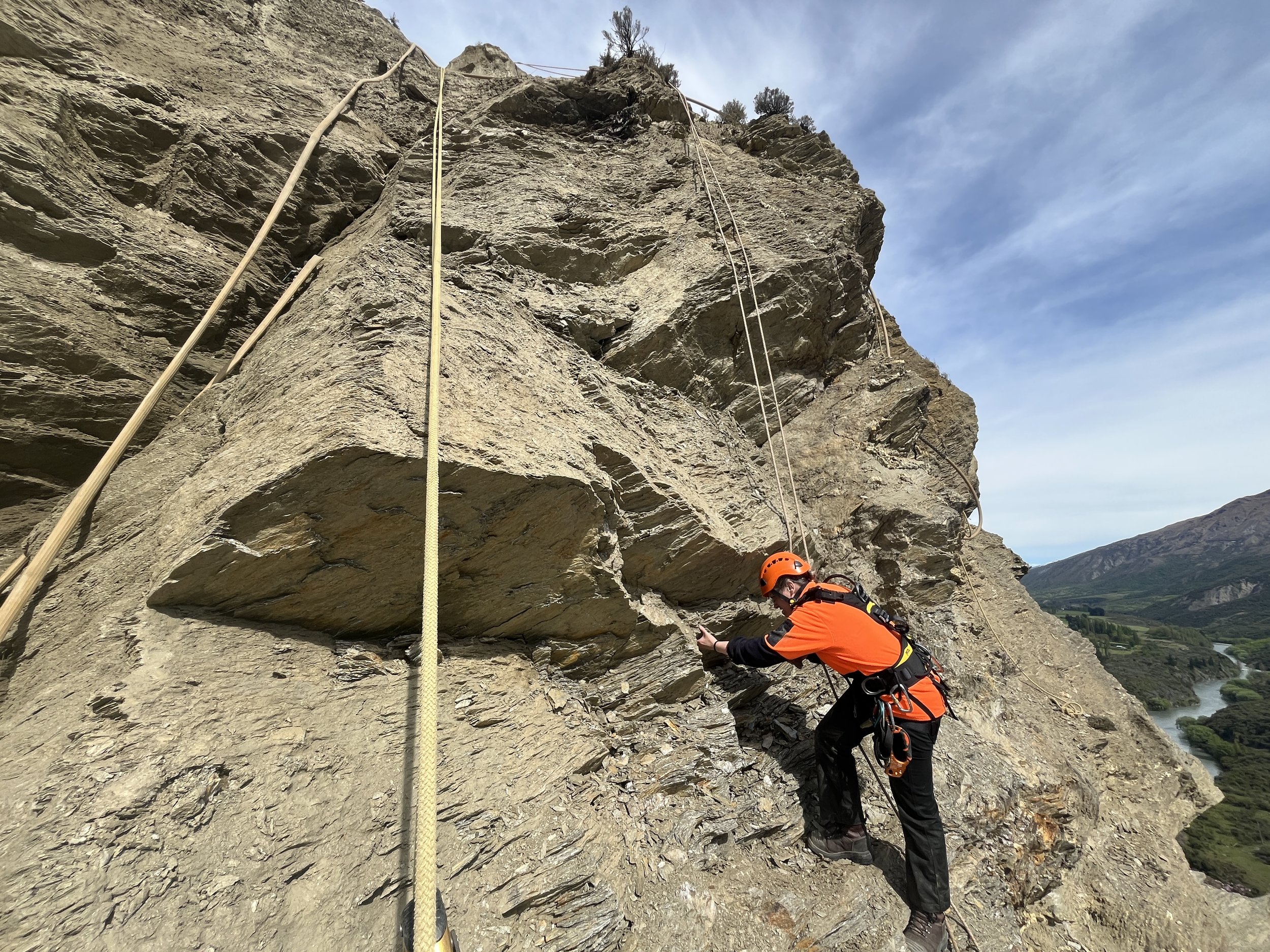 A  person abseiling a rock face with a number of ropes hanging down it.