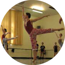 Group of children practicing ballet in a dance studio, some jumping and stretching.