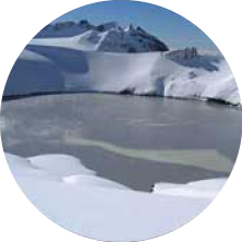 A snowy, icy landscape with glaciers and a frozen body of water under a clear blue sky.