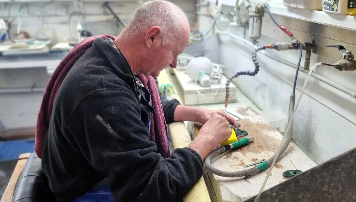 A man in a pounamu workspace cleaning a pounamu pendant.