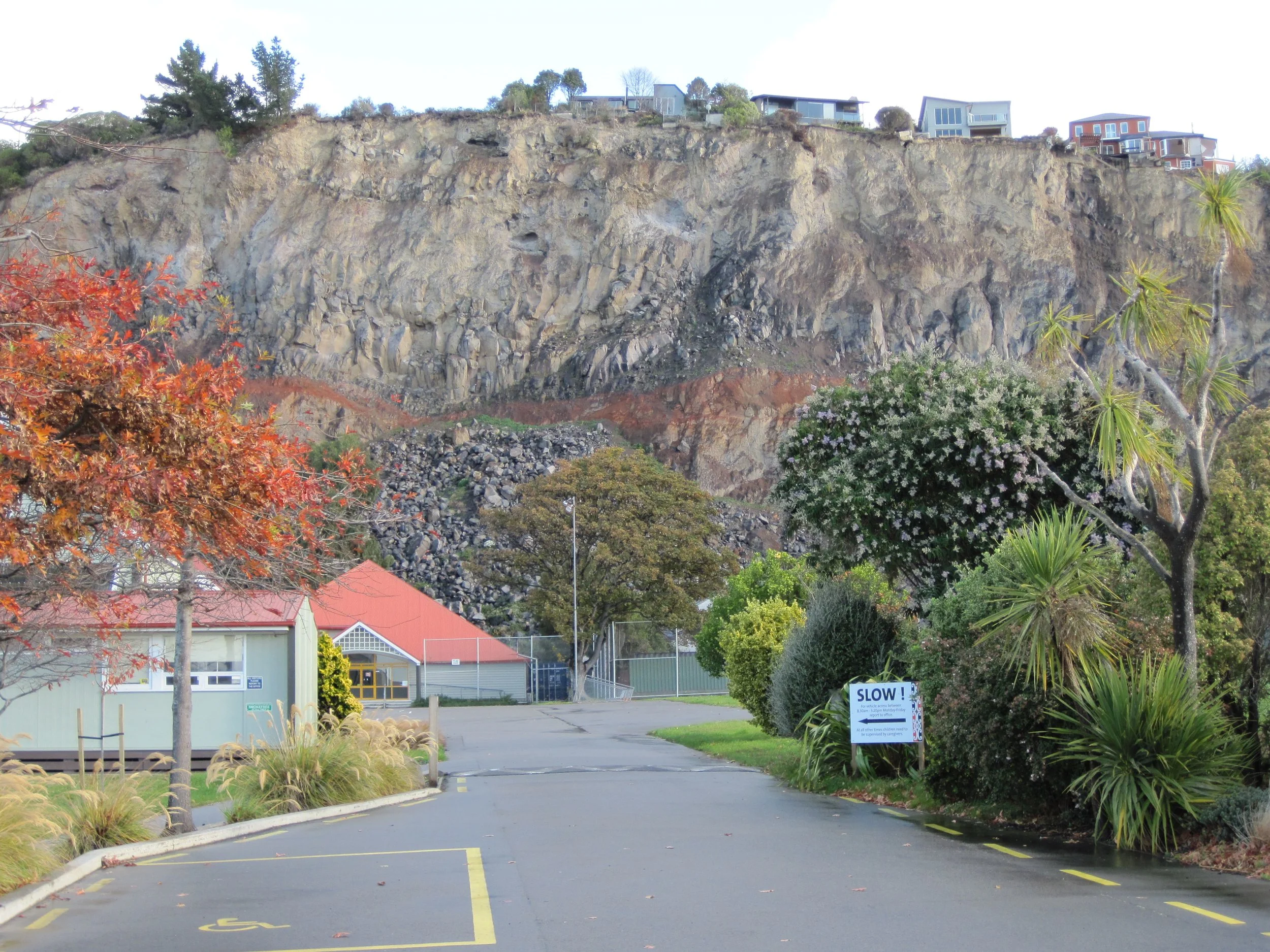 Image of a cliff, with buildings above and below, where a large landslide has occurred.