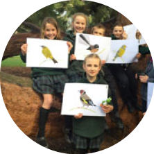 Group of children holding pictures of birds outdoors.