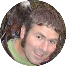 A man smiling with a bird perched on his shoulder.
