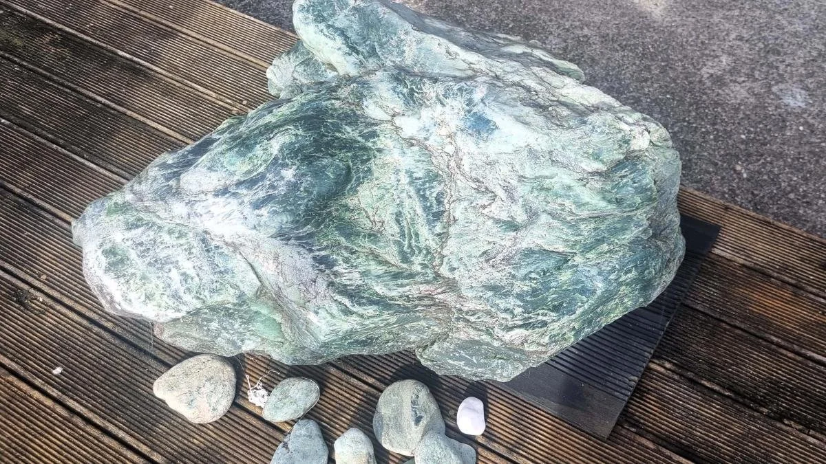 A pounamu rock in its raw form with stones beside it.