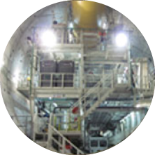 Industrial facility or factory interior with metal stairs, railings, and bright lighting.