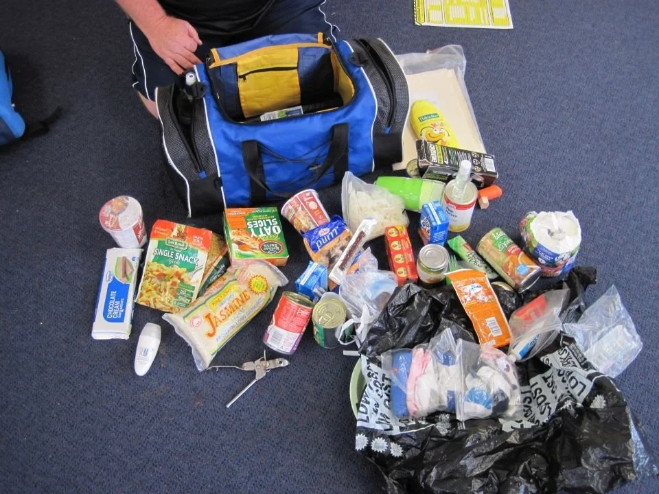 An emergency supply bag with the contents, mainly packaged food, spread out on the floor.