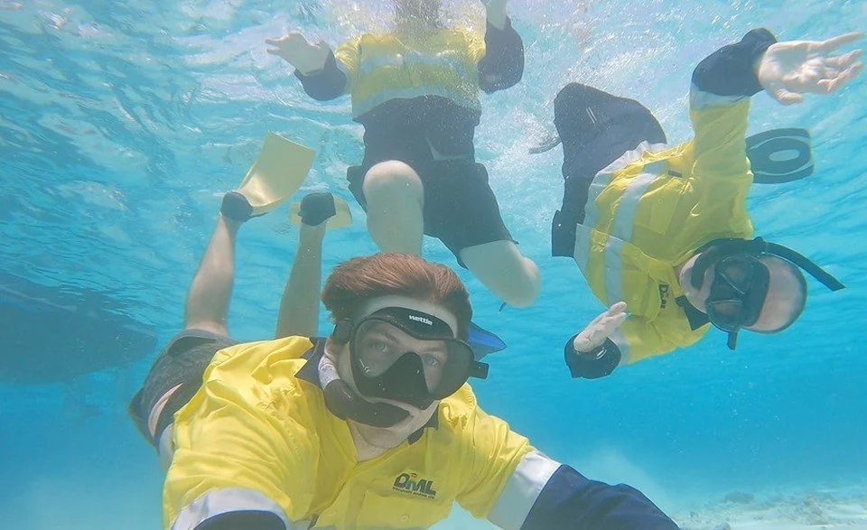 Three people in the water wearing diving masks, snorkels, flippers and hi-vis gear.