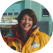 A smiling woman with reddish-brown hair wearing a yellow jacket outdoors.