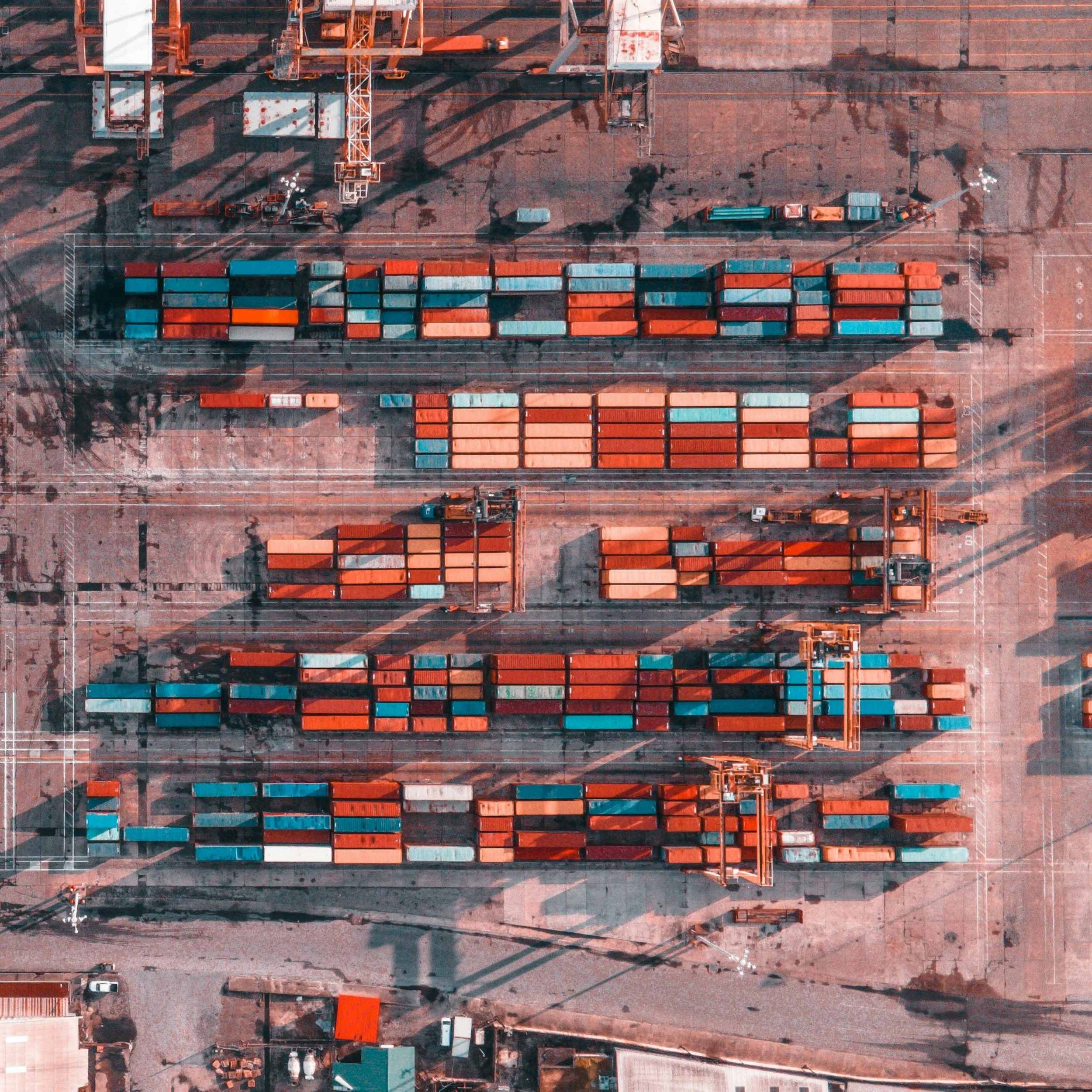Aerial view of a busy global shipping port with stacked containers and cranes – representing international logistics, supply chain management, and worldwide procurement operations