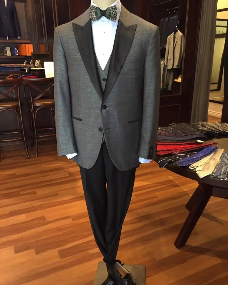 A formal charcoal tuxedo with a textured pattern featuring peak lapels and a feather bow tie