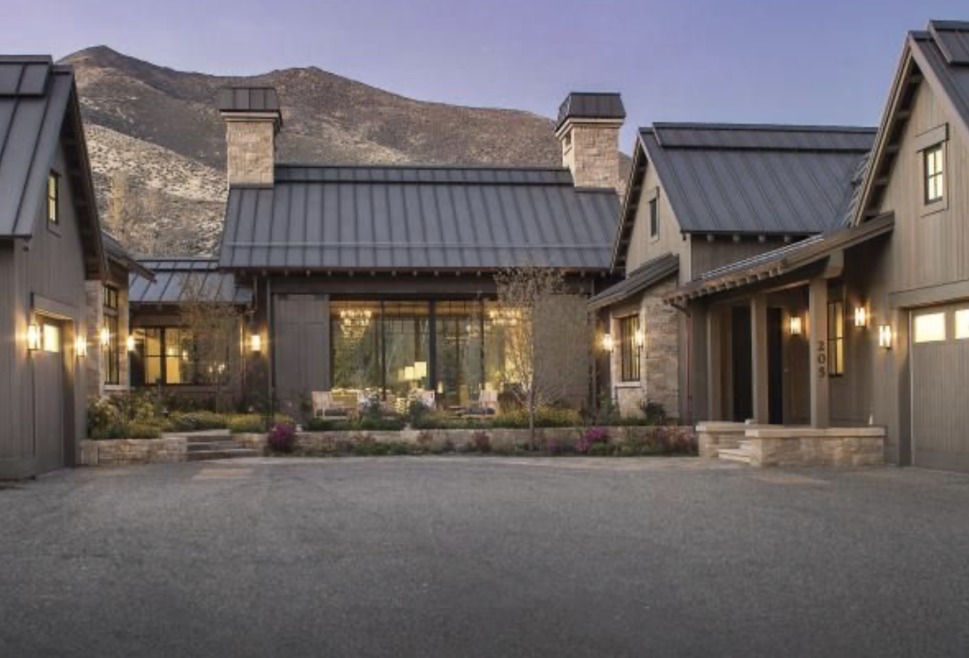 Luxury house with modern design, large windows, and metal roof, situated at the base of a mountain.
