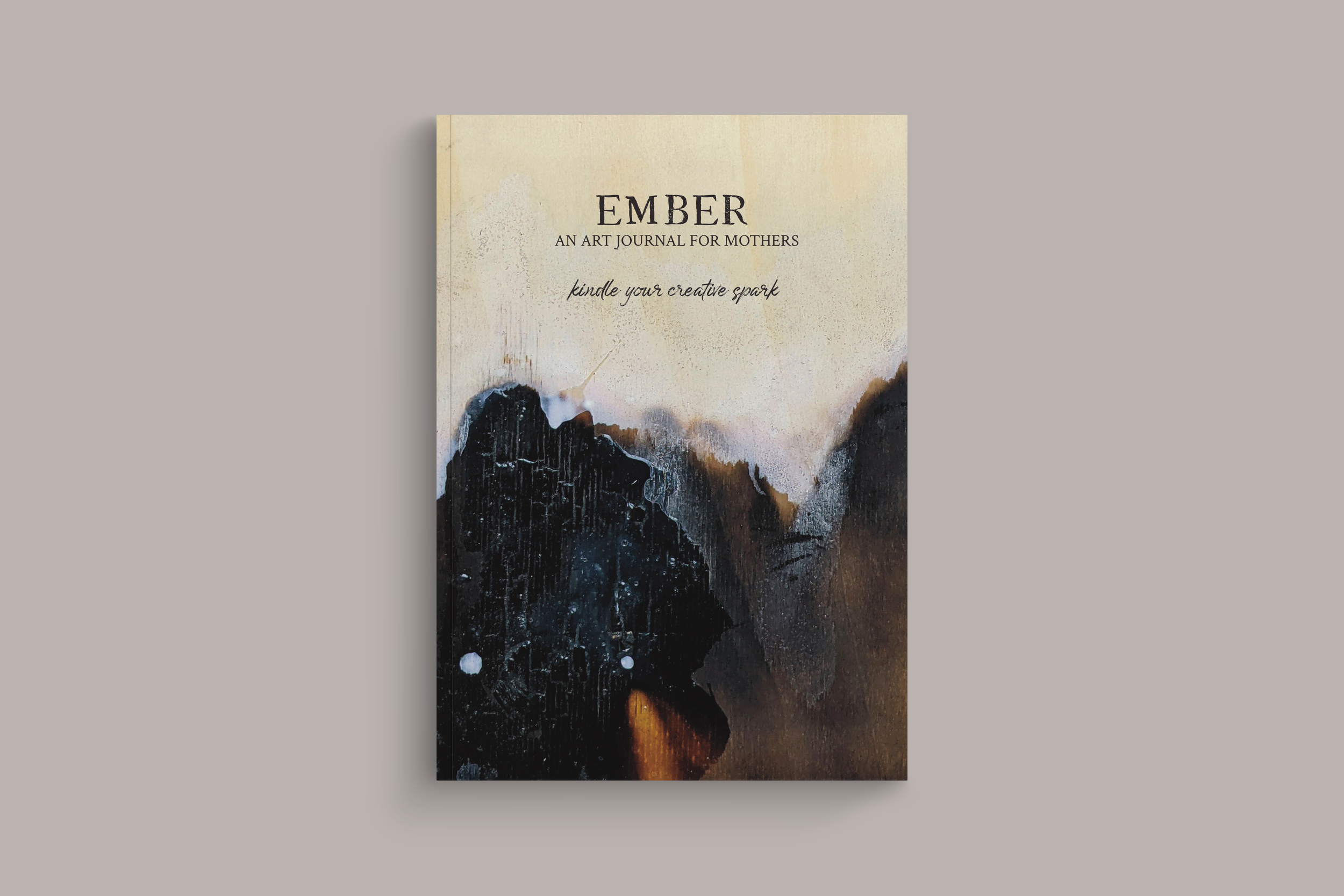  Hardcover copy of Ember: an Art Journal for Mothers to Kindle Their Creative Spark. Cover art is a piece of art created by burning and painting wood. 