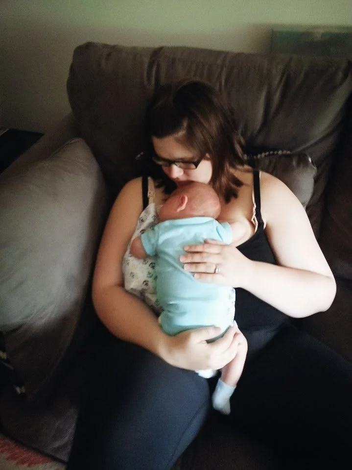 A woman in a nursing tank top sitting on a couch, holding a baby close to her chest