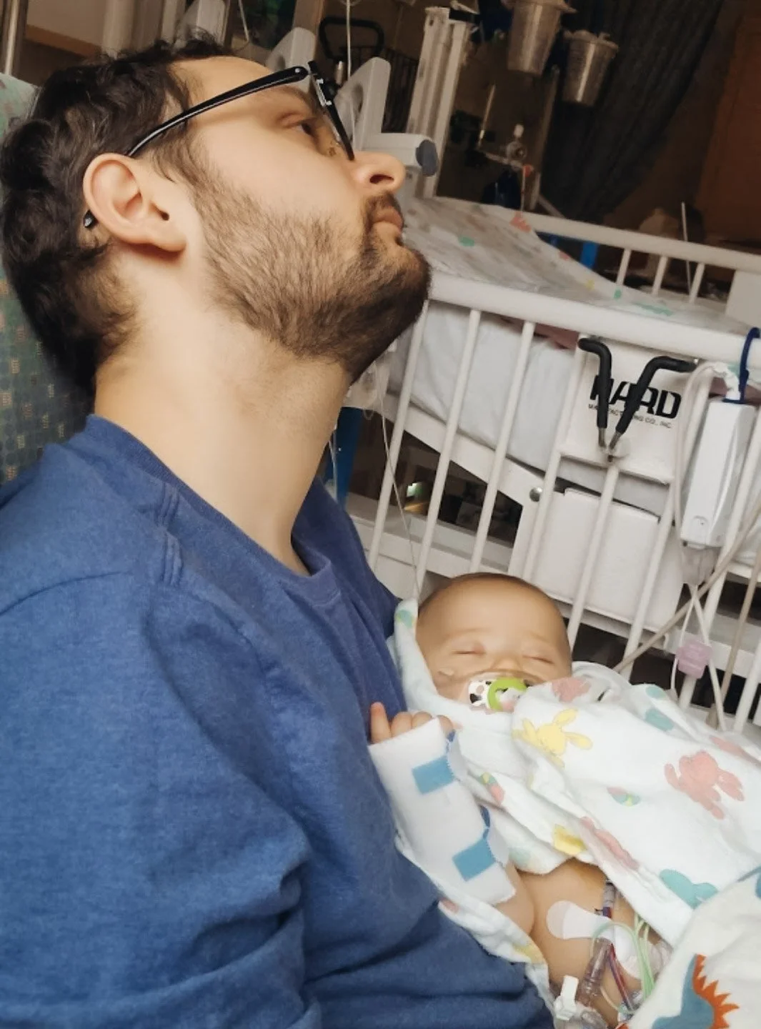 A man sitting in a chair in a pediatric hospital, holding a sleeping baby