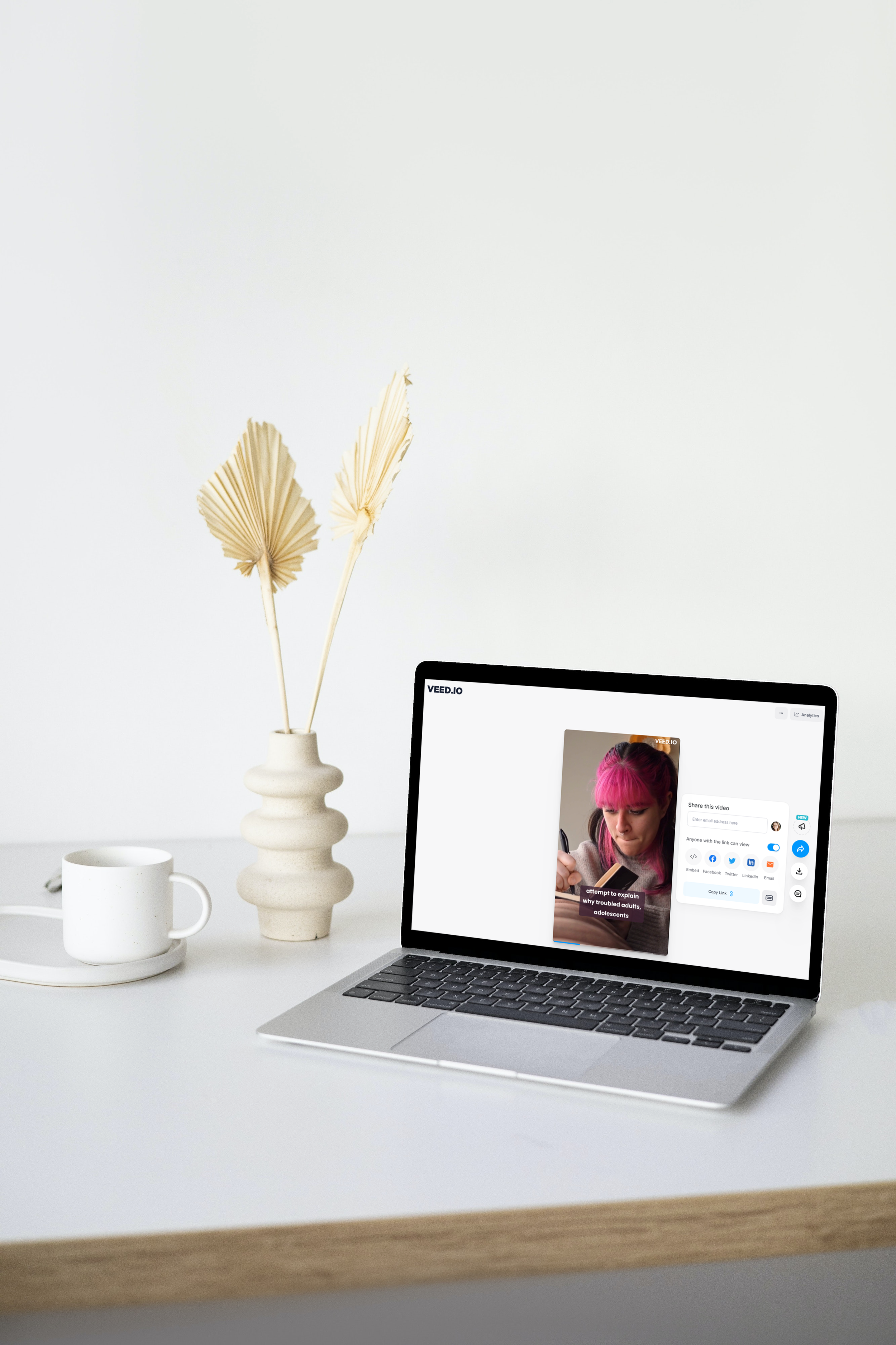 Laptop on a desk next to a vase and tea cup with Veed.io on the screen.