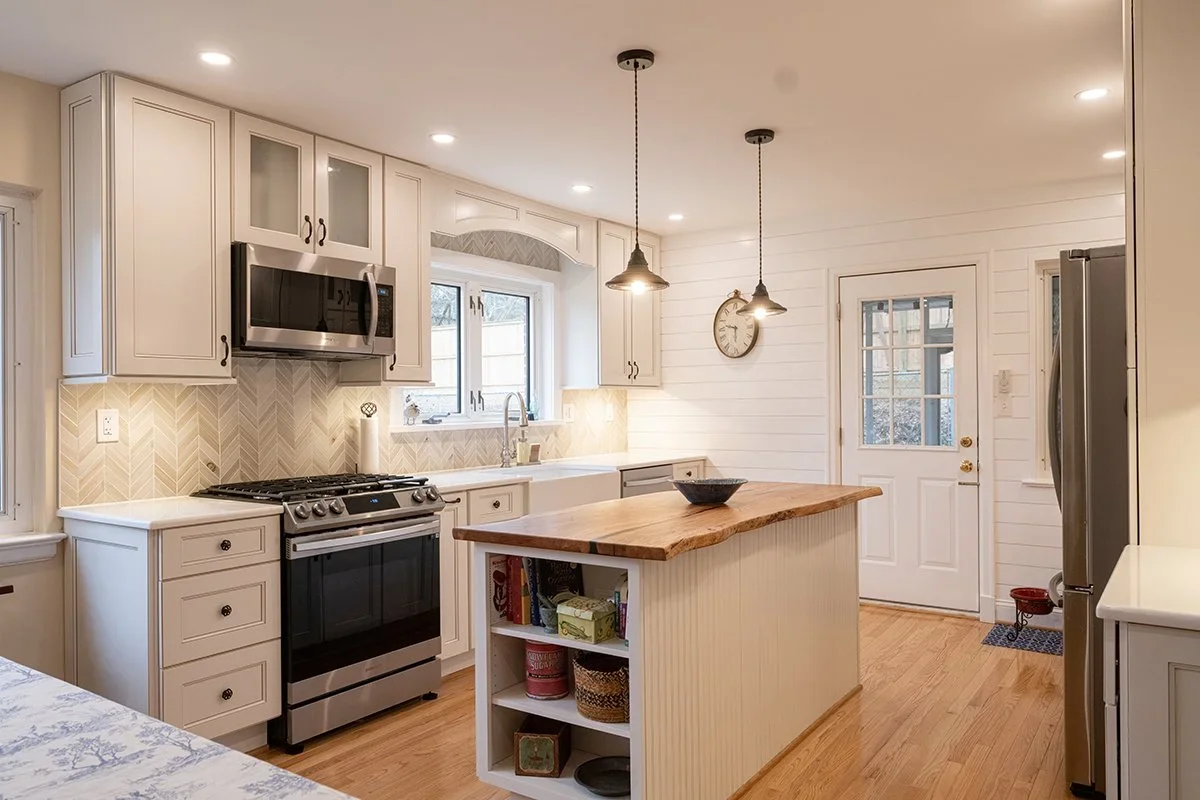 A modern kitchen with white cabinets, stainless steel appliances, a wooden island, and a white shiplap wall.