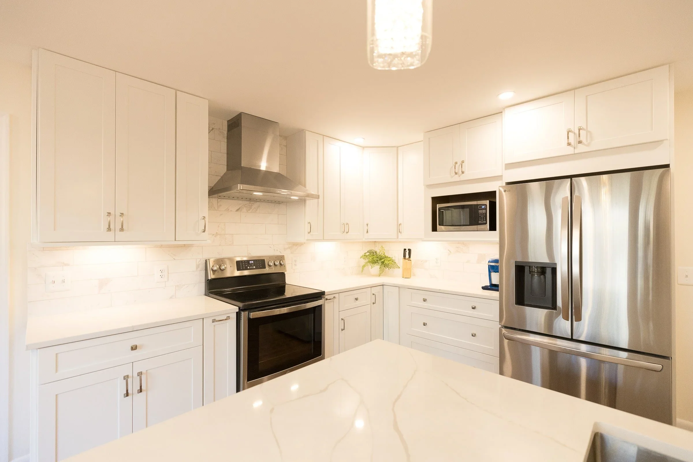 Kitchen with white cabinets, stainless steel refrigerator, stainless steel oven, microwave, and range hood, and a cream-colored marble countertop.