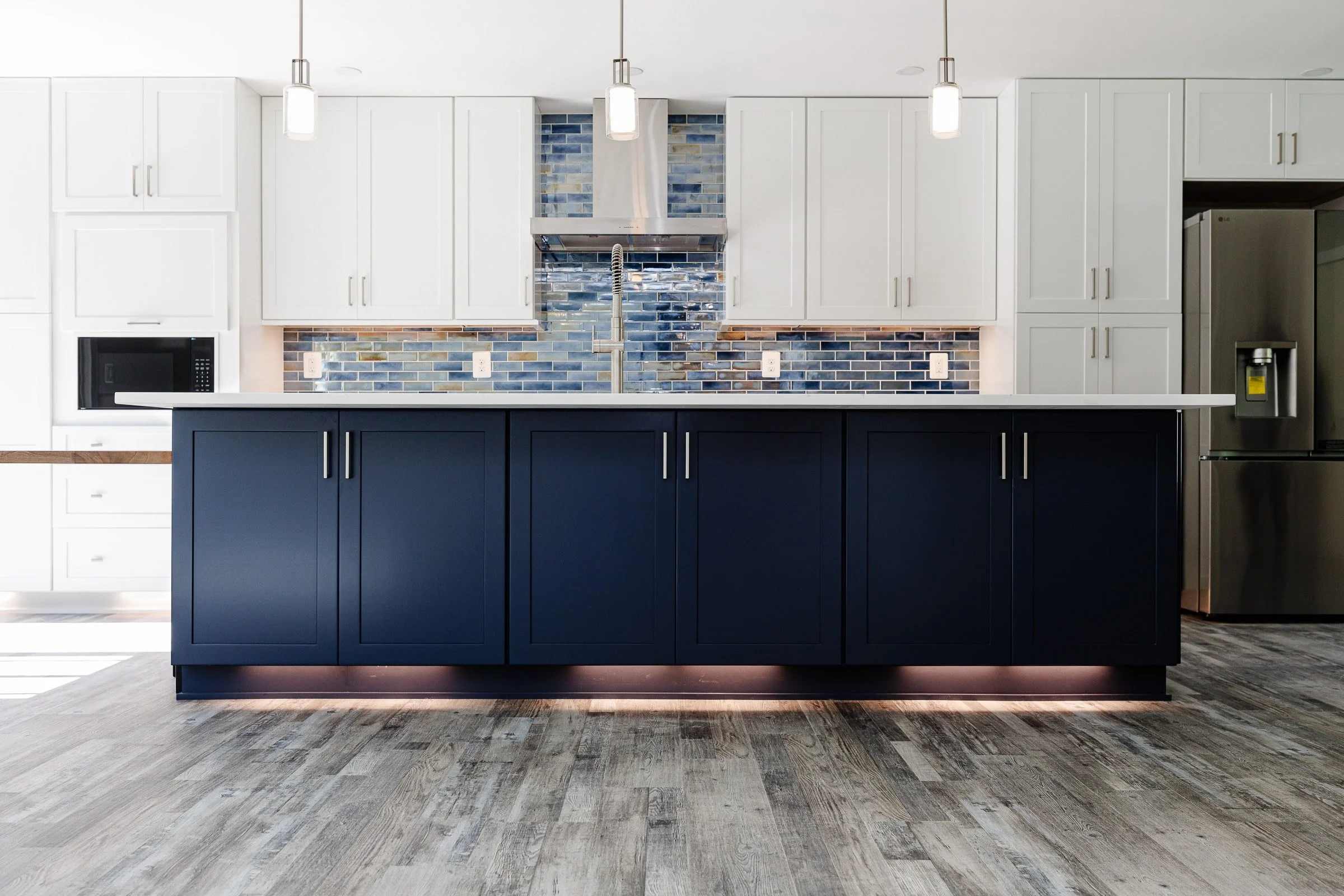 Modern kitchen with white and navy cabinets, blue tile backsplash, and stainless steel appliances.