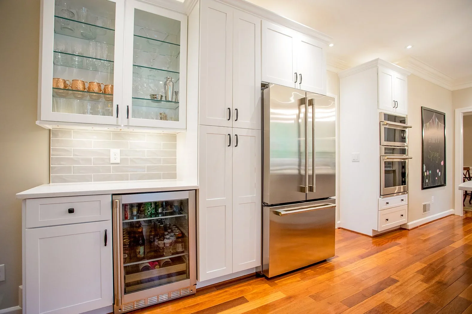 Kitchen with white cabinetry, glass-front upper cabinets, stainless steel refrigerator, built-in microwave, wine cooler, and hardwood floors.