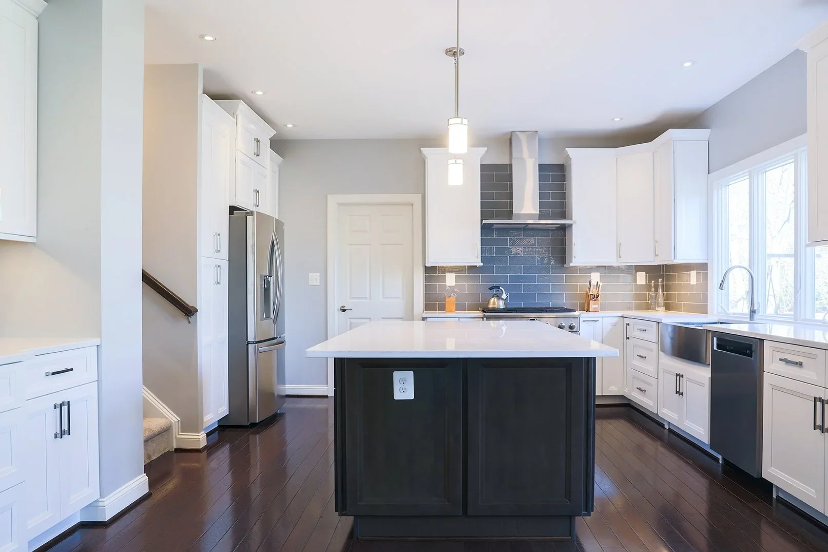 Modern kitchen with white cabinets, black island, stainless steel refrigerator, and dark hardwood floors.