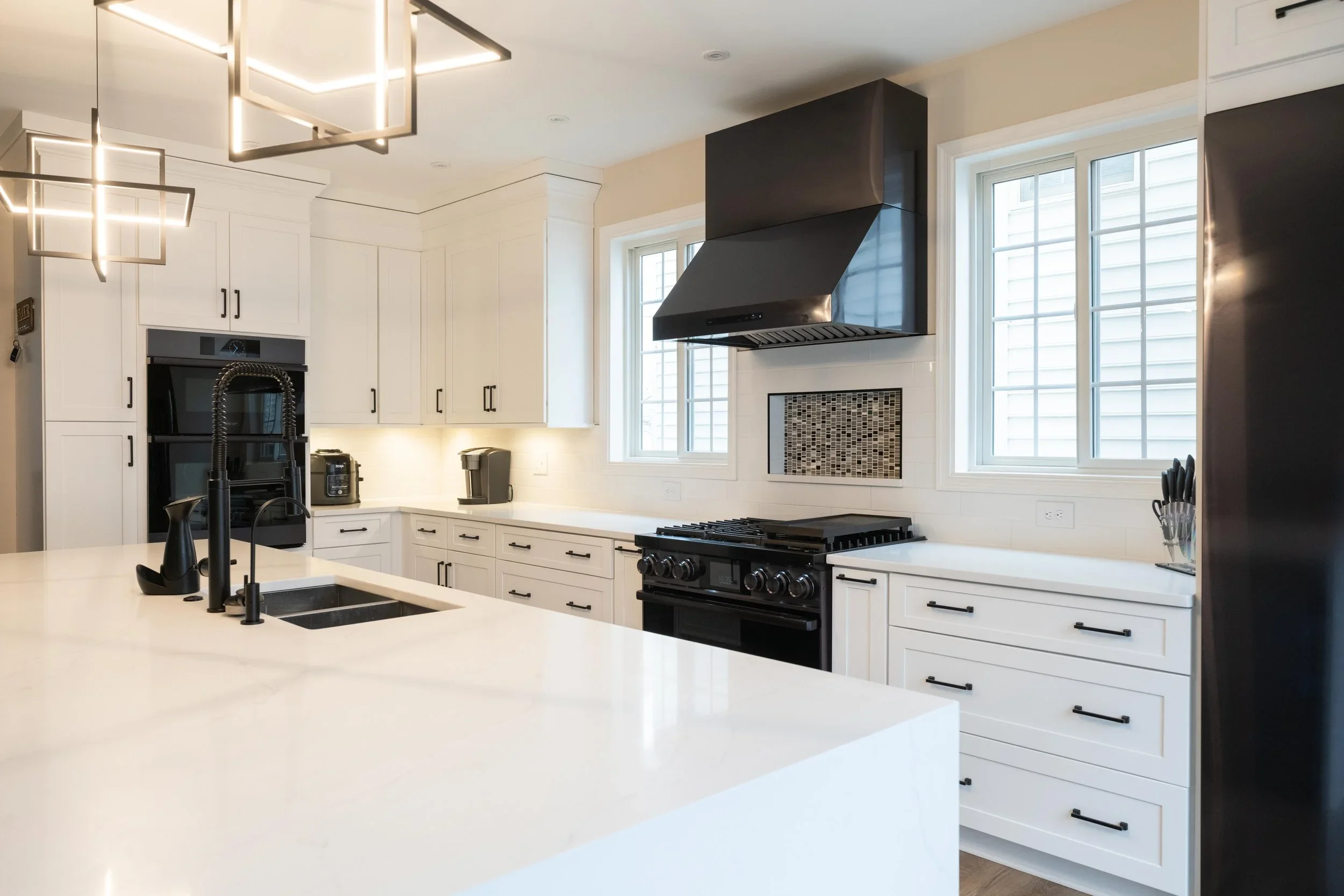 Modern kitchen with white cabinets, black hardware, black range, black range hood, and large windows.