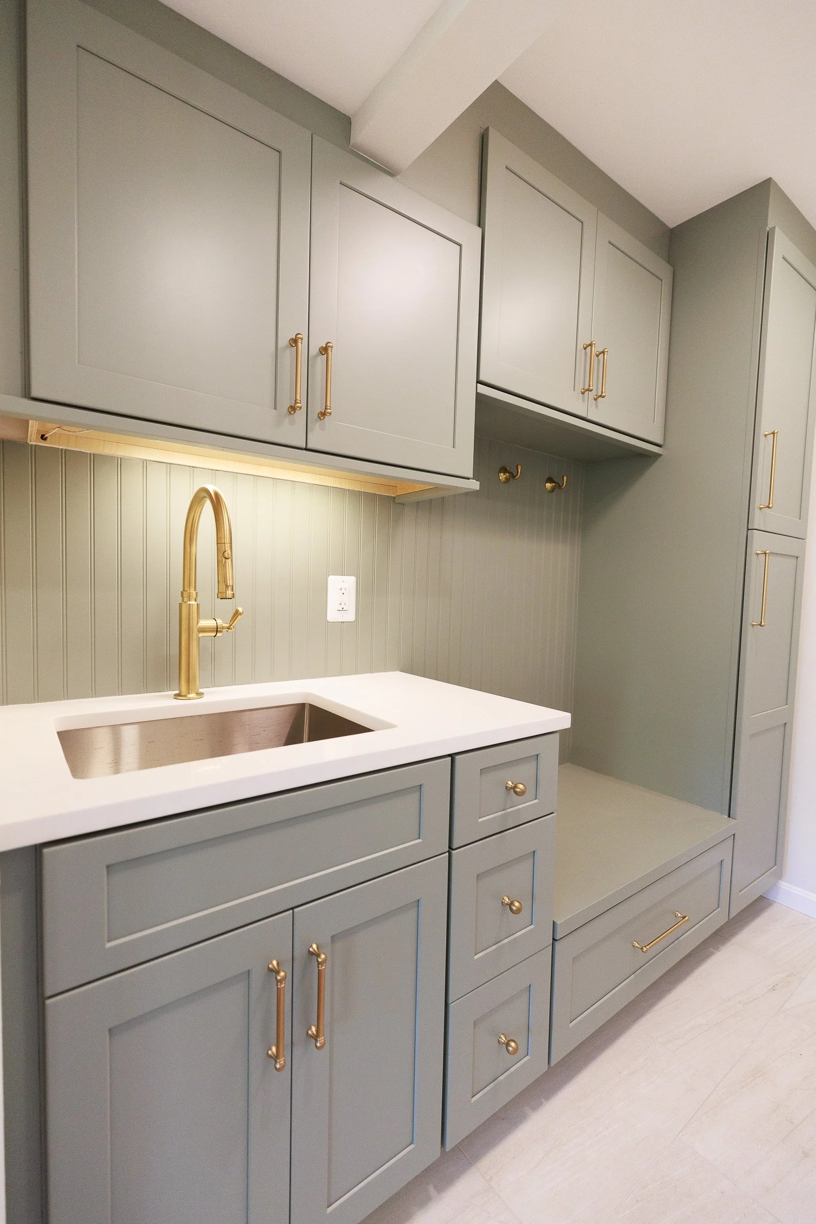 A modern kitchen with gray cabinetry, gold handles, a white countertop, a bronze sink faucet, and a beadboard backsplash.