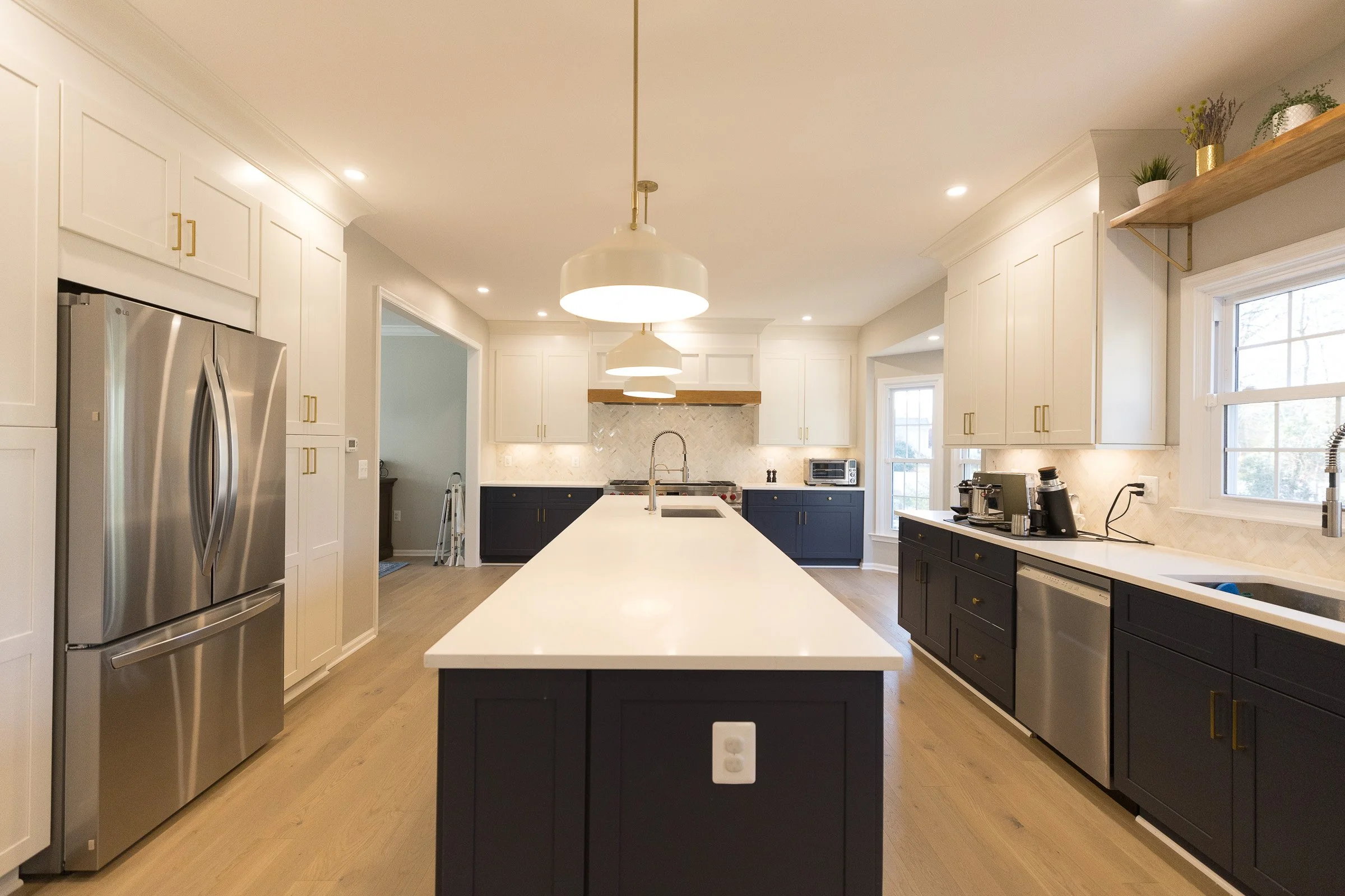 Modern kitchen with white cabinetry, black island, stainless steel refrigerator, and large windows, illuminated by pendant and recessed ceiling lights.