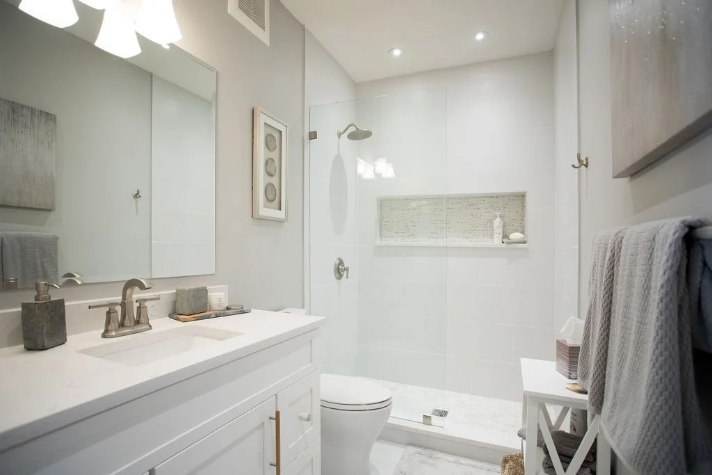 Modern bathroom with white vanity, large mirror, walk-in shower with glass enclosure, tiled shower wall, and neutral gray accessories.