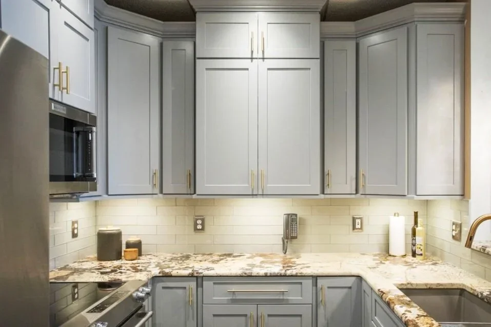 Kitchen with light gray cabinetry, marble countertop, white brick backsplash, stainless steel appliances, and a gold faucet.