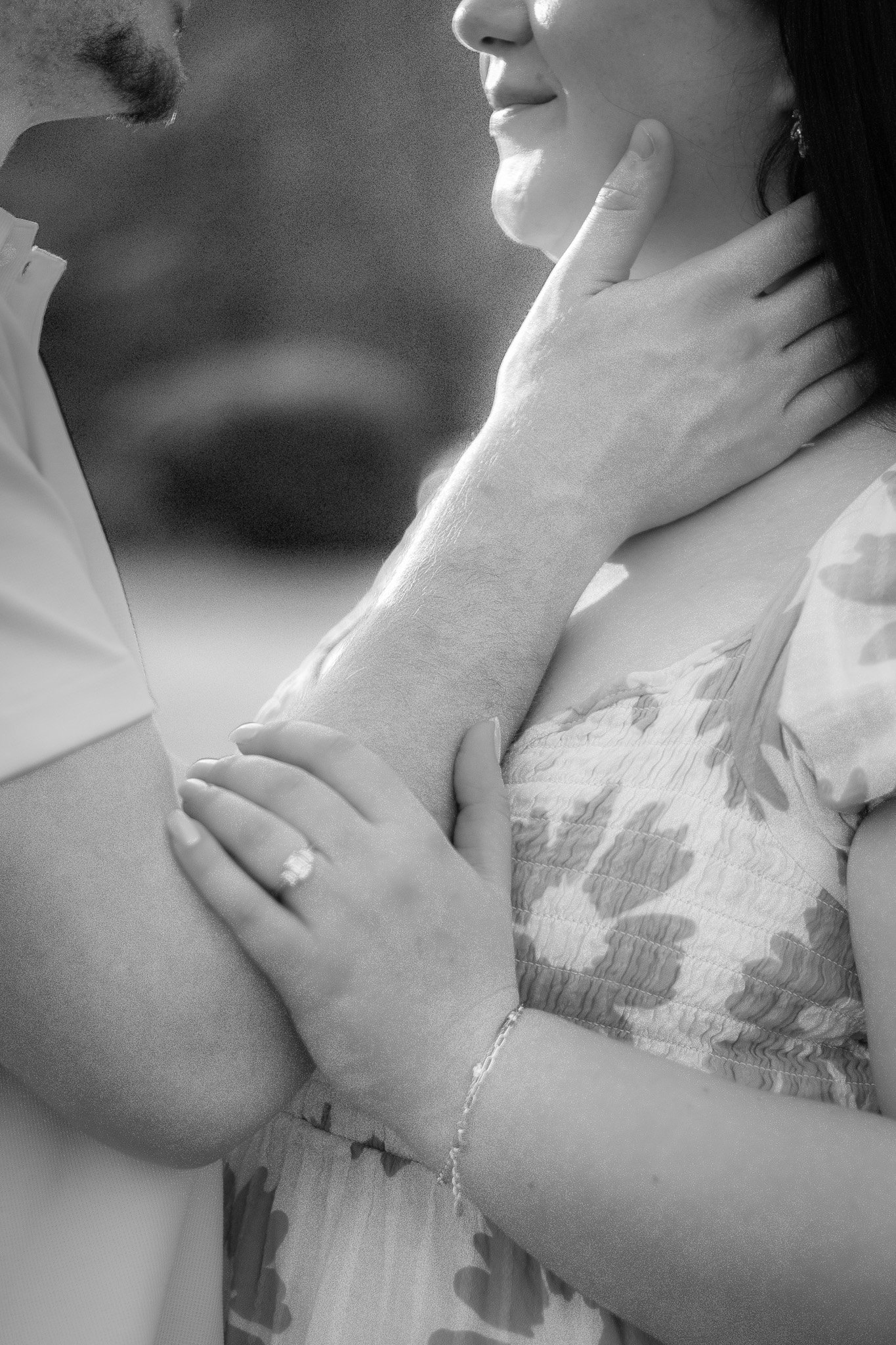 A close-up black-and-white photo of a man and woman facing each other, with the man's hand gently holding the woman's neck and the woman's hand resting on the man's arm, sharing an intimate moment.
