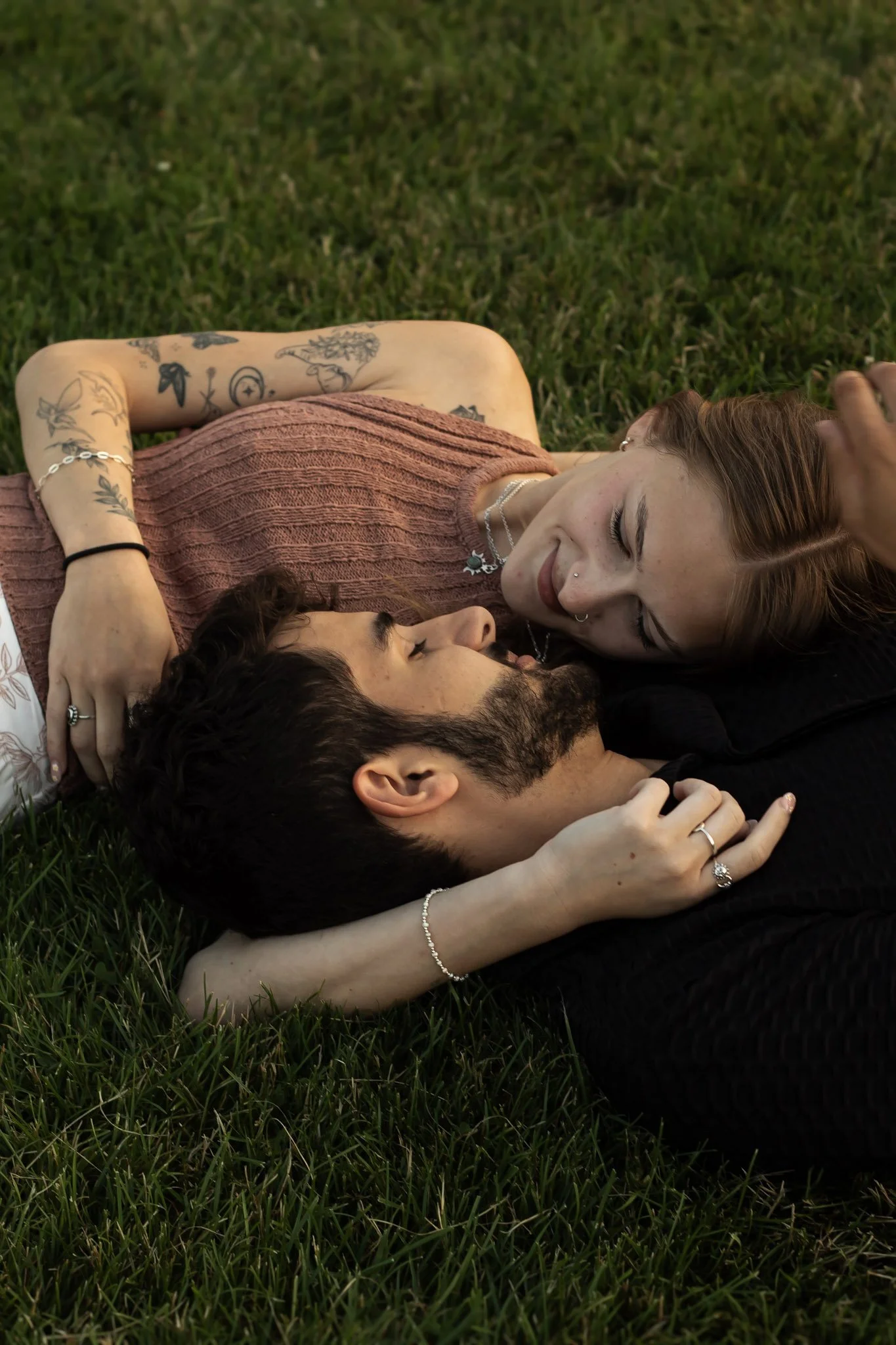 A couple lying on grass, gazing at each other intimately, with their heads close together.
