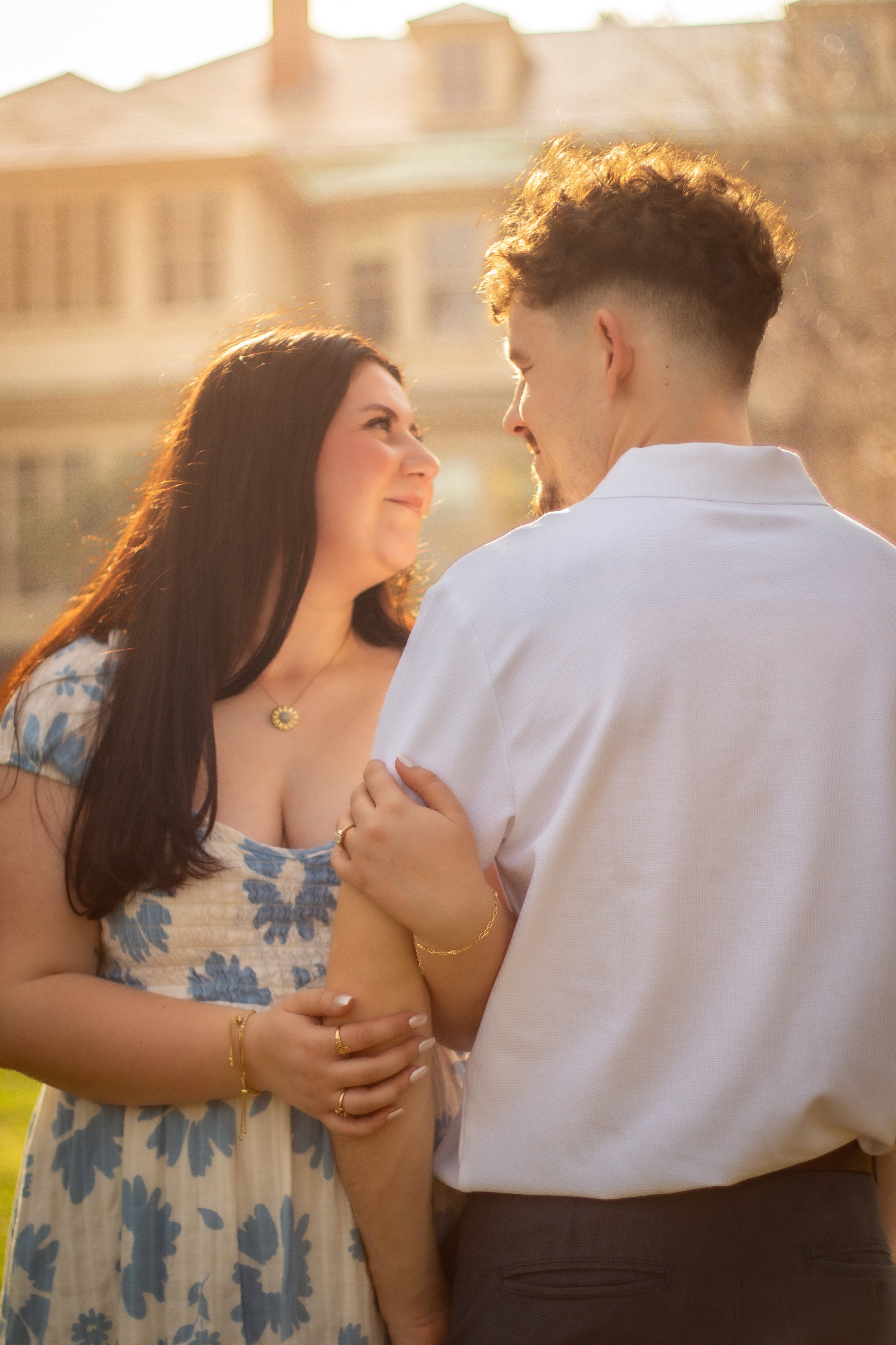 A couple sharing a romantic moment outdoors in warm sunlight, with an elegant house in the background.
